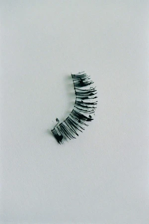 Close-up of a black false eyelash strip on a white surface, showcasing beauty and personal care accessories in a minimalist style.