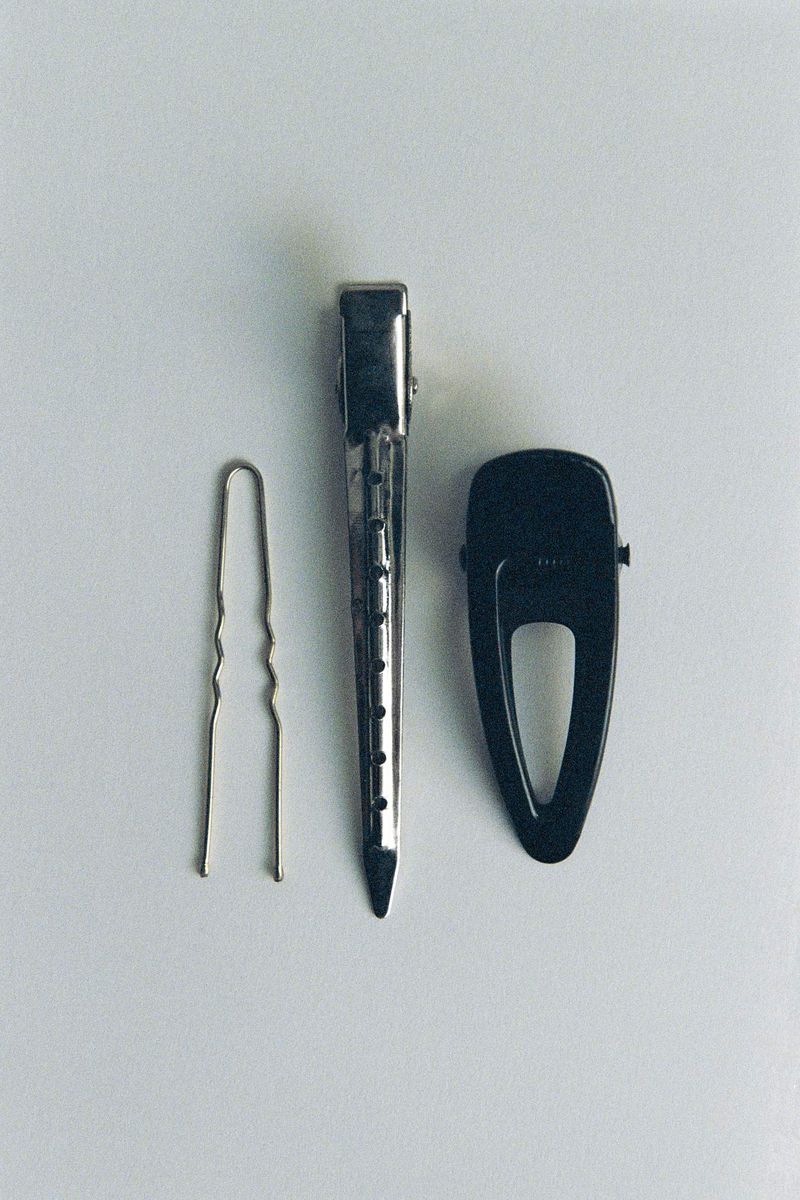 Overhead studio shot of three hair accessories—a bobby pin, an alligator clip, and a snap clip—arranged on a white surface.