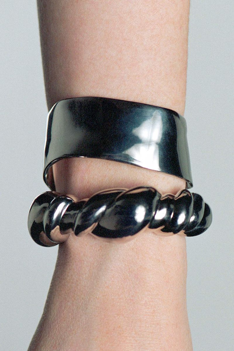 Close-up of a fair-skinned arm adorned with two shiny silver bracelets, one a wide band and the other a twisted rope design.