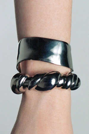 Close-up of a fair-skinned arm adorned with two shiny silver bracelets, one a wide band and the other a twisted rope design.