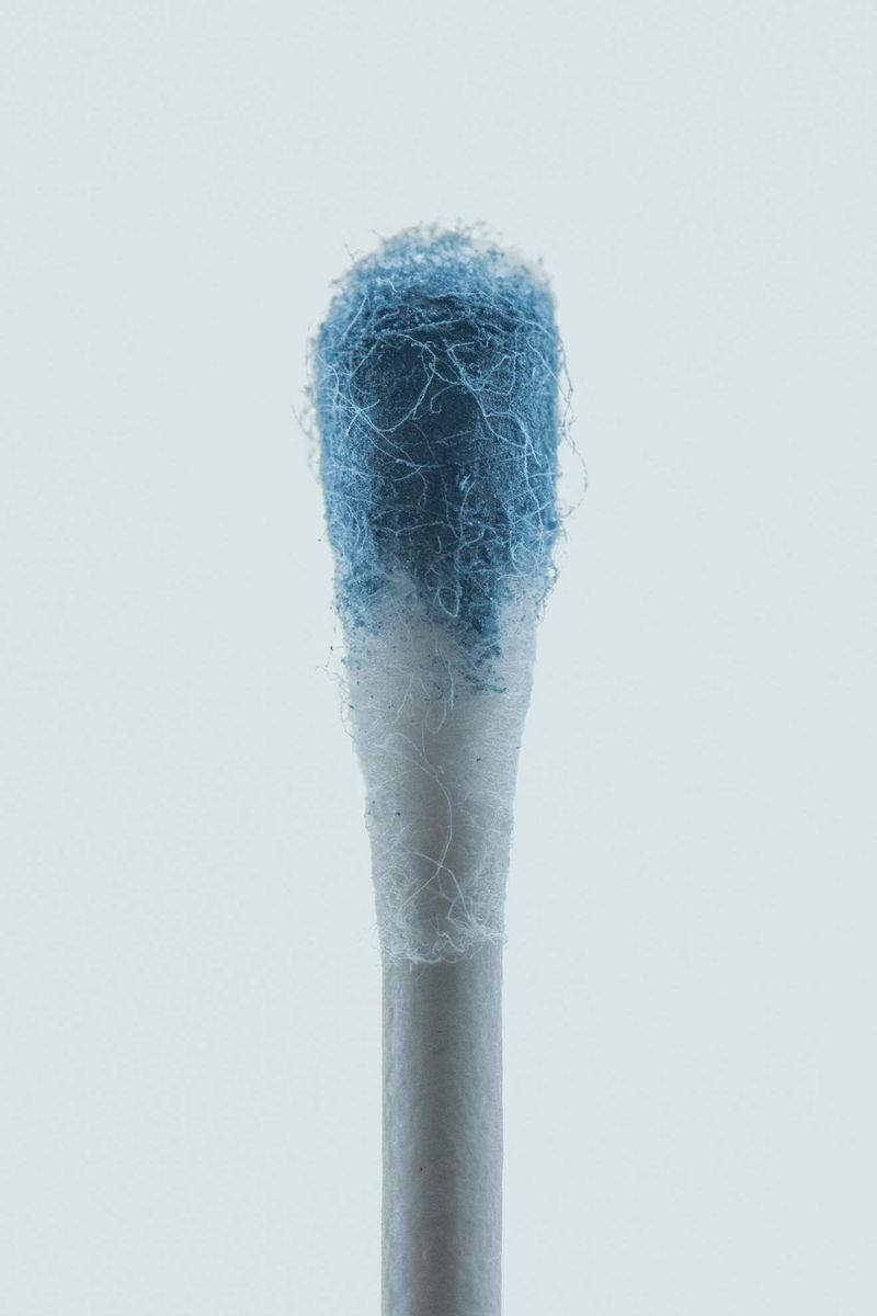 Close-up studio shot of a cotton swab with blue residue on the cotton tip against a light background, focusing on hygiene and healthcare.