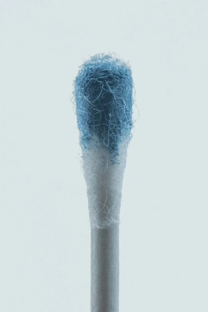Close-up studio shot of a cotton swab with blue residue on the cotton tip against a light background, focusing on hygiene and healthcare.