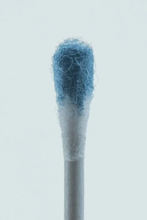 Close-up studio shot of a cotton swab with blue residue on the cotton tip against a light background, focusing on hygiene and healthcare.