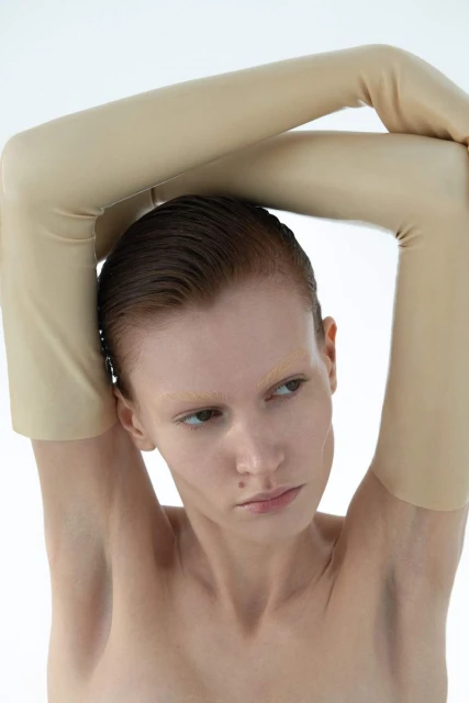 Close-up portrait of a light-skinned adult woman in beige gloves looking away with a neutral expression against a white backdrop.