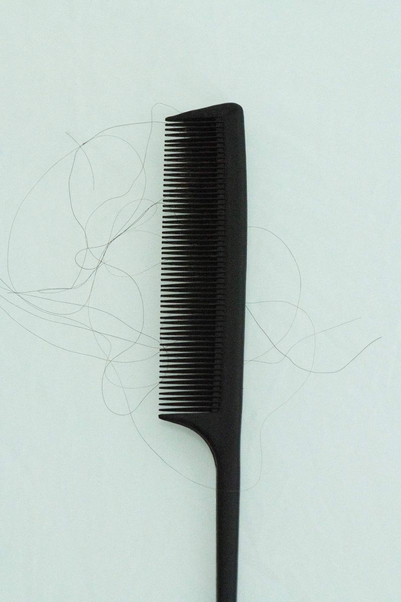 Close-up shot of a black comb with several strands of hair on a light background, showcasing hair care and personal grooming.