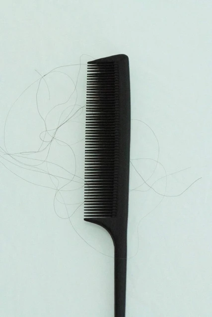 Close-up shot of a black comb with several strands of hair on a light background, showcasing hair care and personal grooming.