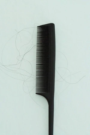 Close-up shot of a black comb with several strands of hair on a light background, showcasing hair care and personal grooming.
