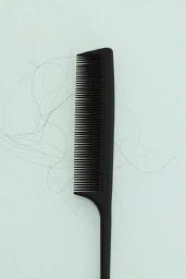 A black tail comb resting on a light background with stray strands of hair tangled in its teeth.