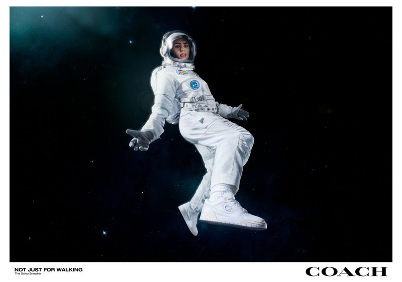 A person in a white space suit floats against a dark, starry background, wearing white sneakers, promoting the Coach Soho Sneaker.