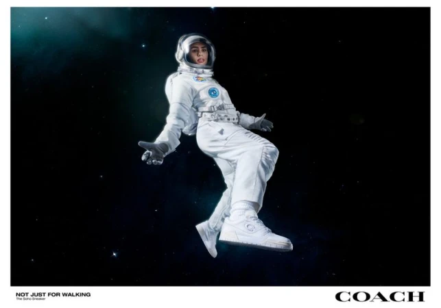 A person in a white space suit floats against a dark, starry background, wearing white sneakers, promoting the Coach Soho Sneaker.