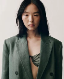 Portrait of a model wearing an olive green blazer and matching top against a neutral light background for Mango