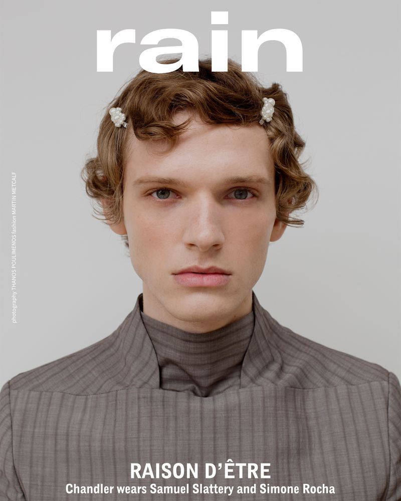 Close-up studio shot of a fair-skinned adult male model wearing a gray pinstripe turtleneck, styled with hair clips, with 'rain' logo above.