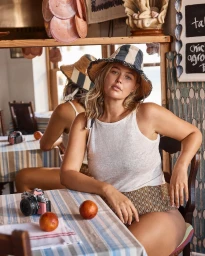 Woman wearing a striped hat and white top sitting at a table with oranges and a vintage camera in a cafe