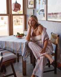 Woman in striped linen loungewear seated at a table inside a sunlit café for a Women’s Weekly Australia editorial project.