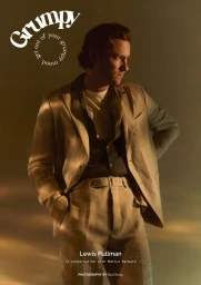 Actor Lewis Pullman wearing a neutral beige suit and dark shirt against a warm lit background for Grumpy Magazine.