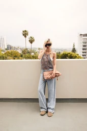 Model in oversized sunglasses wearing a patterned halter top, light wash jeans, and holding a pink clutch on a rooftop.
