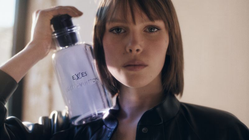 Portrait of a young adult woman holding a Louis Vuitton fragrance bottle, in a close-up studio setting with diffused natural light.