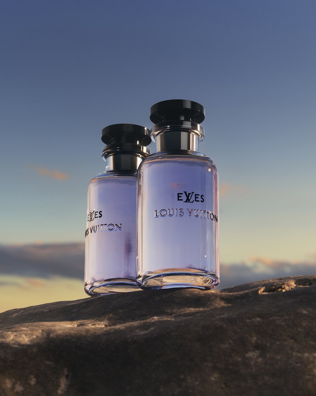 Two Louis Vuitton fragrance bottles sit on a rock formation under a twilight sky, showcasing the brand's luxury and natural setting.