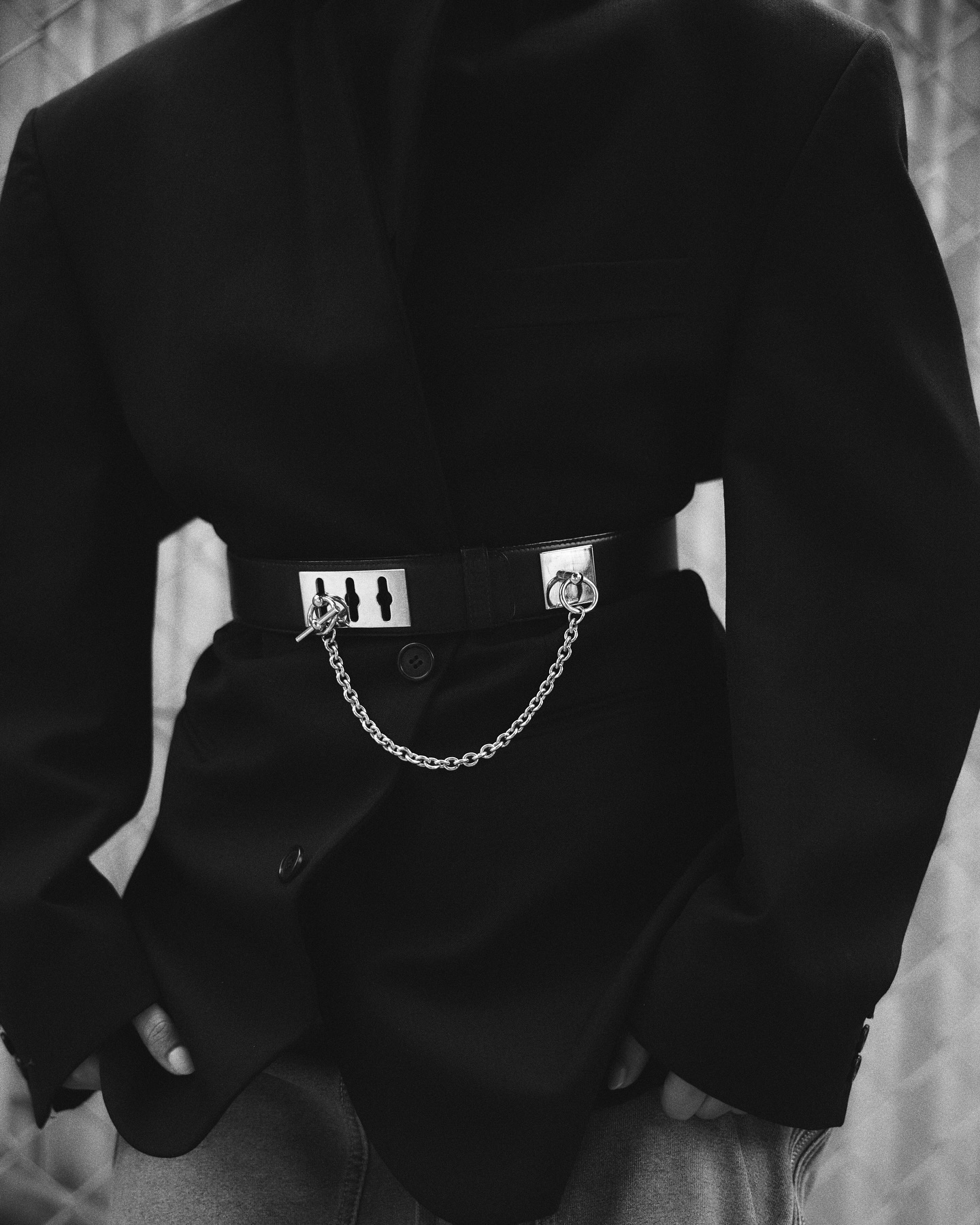 Black and white portrait of a person wearing a blazer, black belt with silver details, and jeans, posing in an indoor setting.