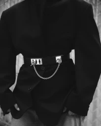 Close-up of a person wearing a black blazer and a wide black belt with silver hardware and a chain link detail.