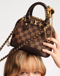 Louis Vuitton Damier canvas handbag balanced on a person's head with a gold chain strap against a white background