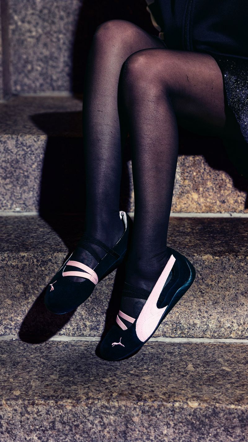 Close-up of legs wearing black tights and Puma Speedcat sneakers seated on stone steps.