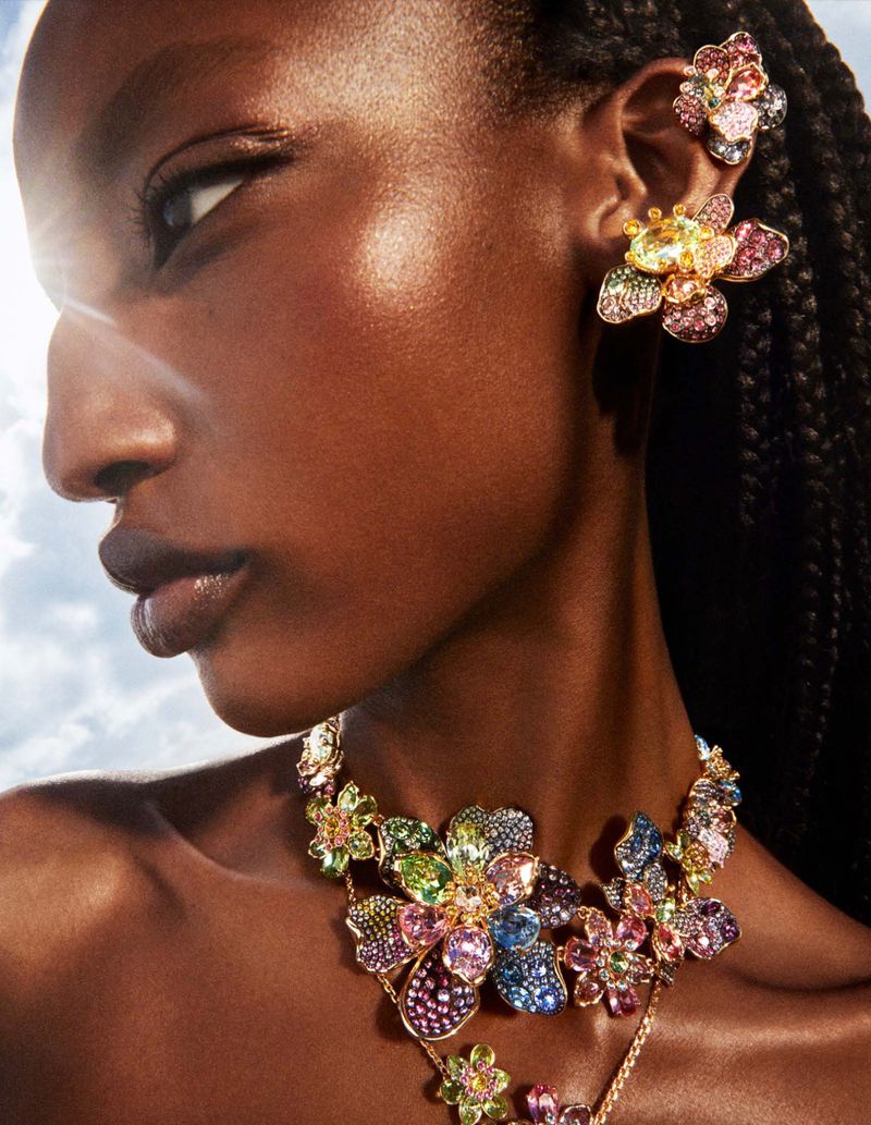 Close-up of a woman wearing a floral jeweled ear cuff and necklace against a sky-like backdrop, showcasing fashion jewelry.