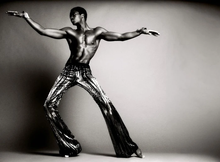 Model Alton Mason striking a dynamic pose in sparkling metallic trousers against a grey gradient background for V Magazine