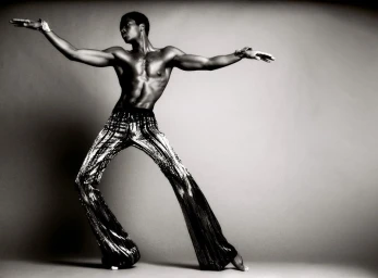 Model Alton Mason striking a dynamic pose in sparkling metallic trousers against a grey gradient background for V Magazine