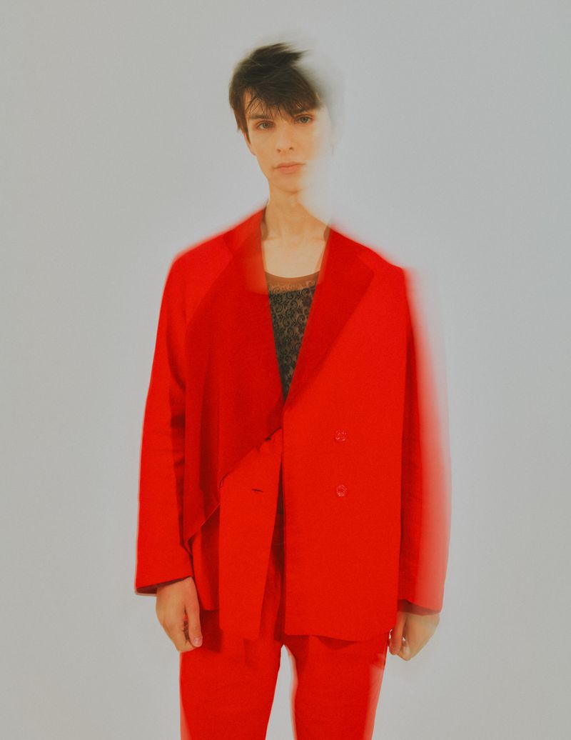Person in a red suit poses against a neutral background with a blurred effect. Fashion and style concept. Neutral expression.