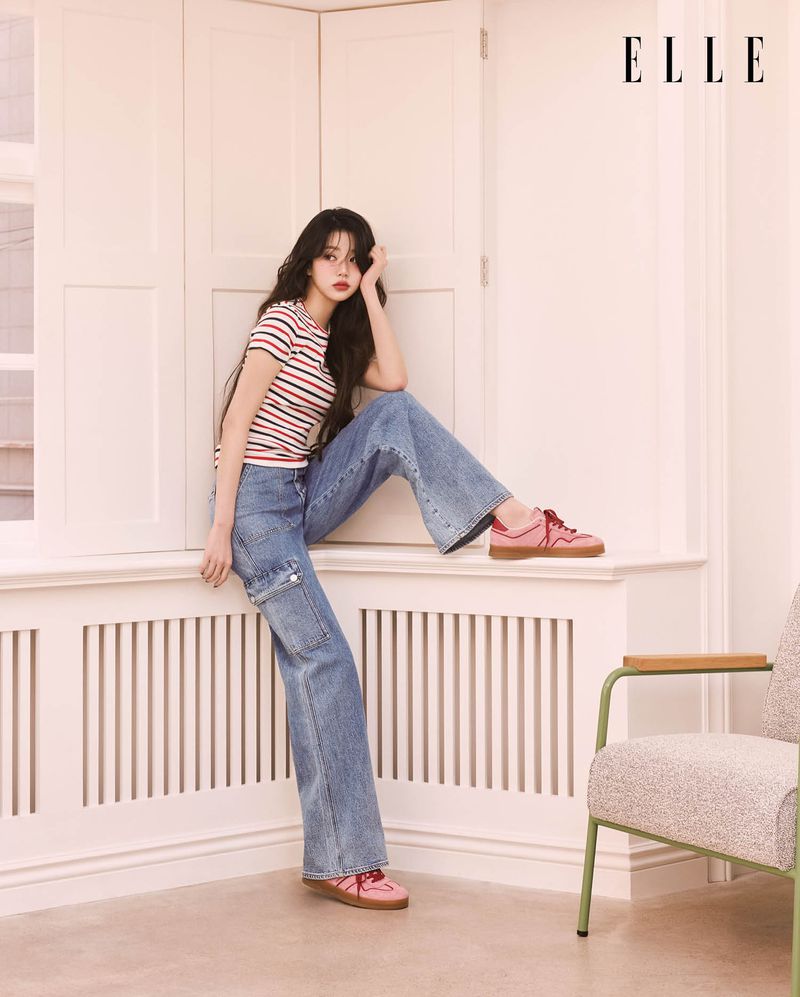 A stylish woman with long dark hair wearing jeans and a striped shirt sits on a windowsill in a fashion editorial shot with "ELLE" logo.