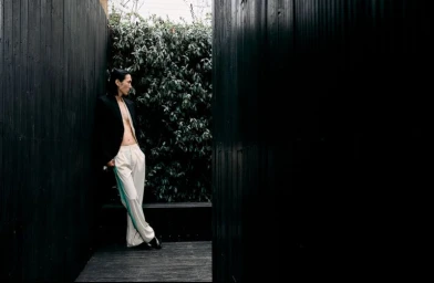 Model Hyuk Kim wearing an open black blazer and light trousers leaning against dark wooden walls in the Clock-out Chronicles project.