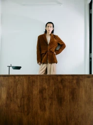Model Hyuk Kim wearing a brown corduroy blazer behind a wooden desk in the Clock-out Chronicles project.