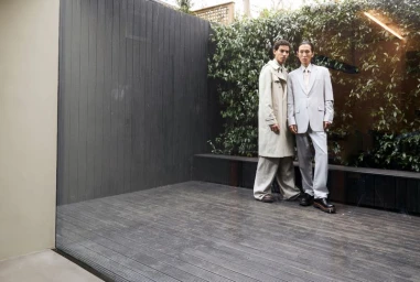 Two male models standing on a wooden patio against a dark paneled wall and leafy foliage for Hashtag Legend Clock-out Chronicles.