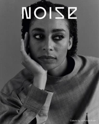 Portrait of singer Celeste resting her chin on her hand, wearing a grey textured top against a solid grey background