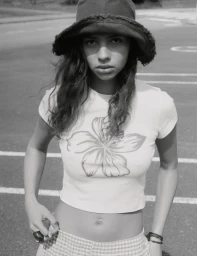 Monochrome portrait of a young woman wearing a bucket hat and floral crop top outdoors on asphalt.
