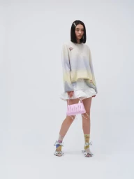 Model wearing a gradient sweater and white ruffled shorts holding a pink handbag against a white background