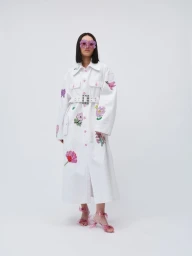 Model in white belted coat with floral appliqués and pink flower sunglasses against a seamless white background.