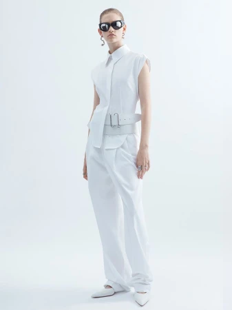 Fashion model in a white sleeveless shirt, wide-leg pants, and sunglasses poses in a bright, neutral studio setting for a fashion shoot.