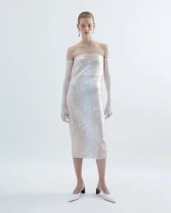Model wearing a strapless sequin dress and white gloves against a plain white studio background.