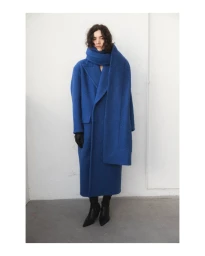 Model in a bright blue long coat and matching scarf standing against a plain white wall.
