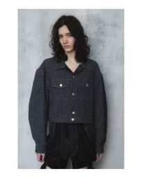 Model wearing a dark textured cropped jacket with silver buttons against a mottled grey wall