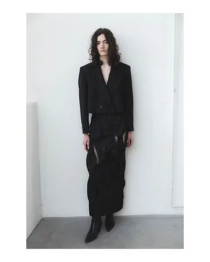 Model wearing a black tailored jacket and cutout maxi skirt standing against a plain white wall