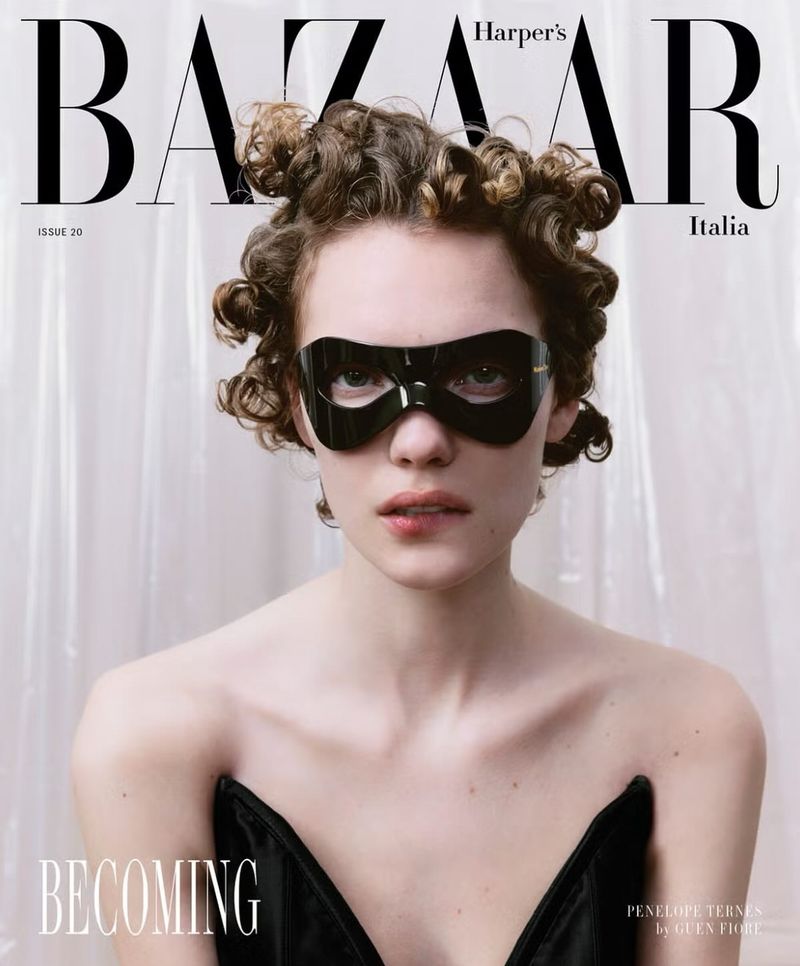 Harper's Bazaar Italia cover featuring a woman with curly hair wearing a black mask and a black corset against a white backdrop.