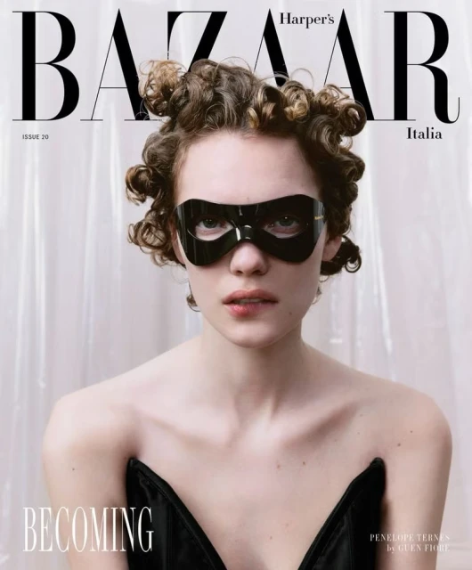 Harper's Bazaar Italia cover featuring a woman with curly hair wearing a black mask and a black corset against a white backdrop.