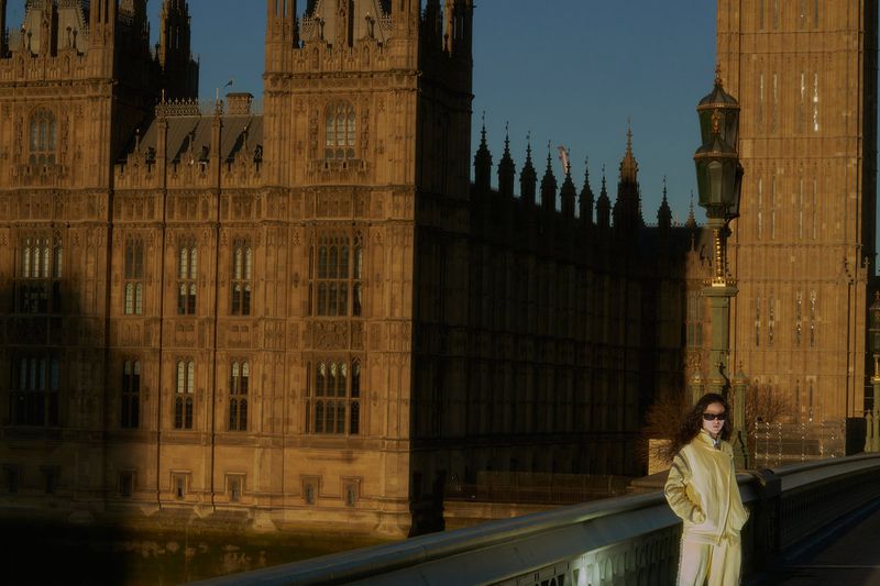 Adult female in London, England, posing in front of the Houses of Parliament and Elizabeth Tower (Big Ben) on a bridge in daylight.