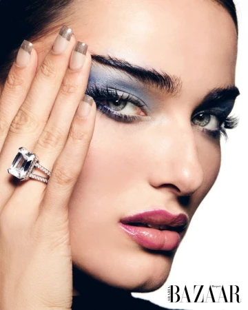 Close-up fashion shot of an adult woman with smokey blue eyeshadow, glossy pink lipstick, and large diamond ring posing in studio.