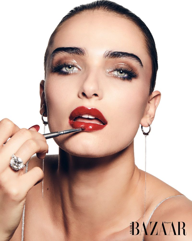 Close-up shot of a woman applying red lipstick with a brush, enhancing her beauty look. The image is against a white backdrop.