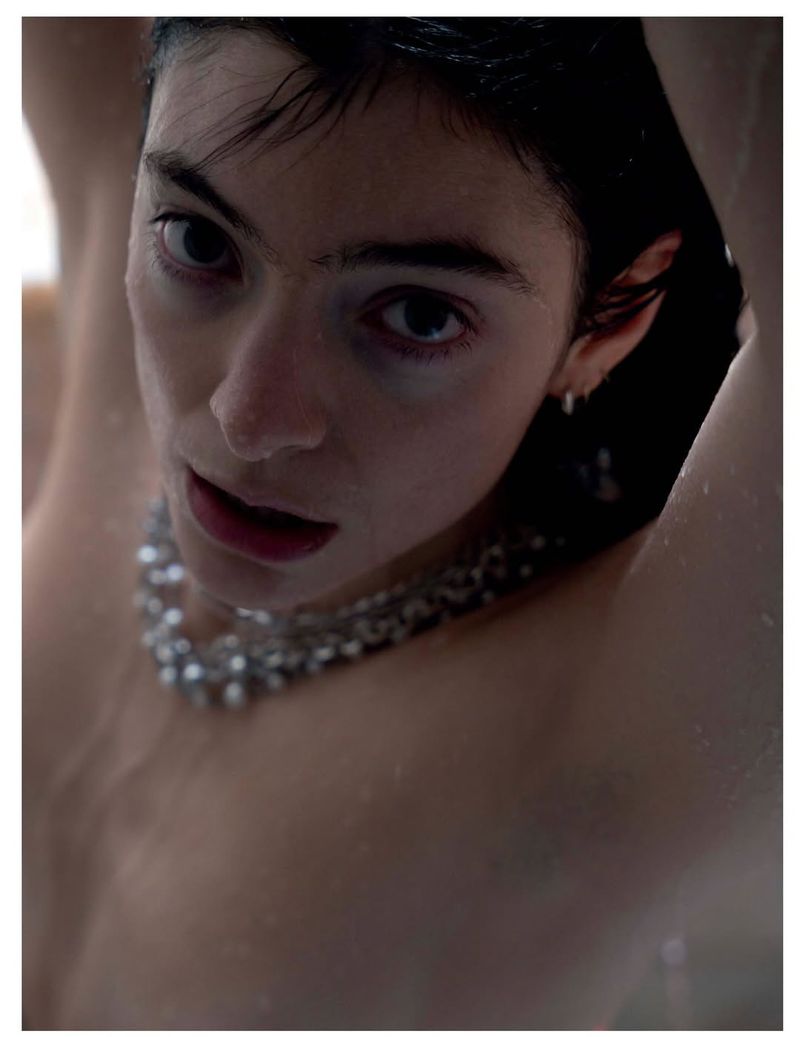 Close-up portrait of a young adult with dark hair looking up, wearing a beaded necklace, and lit with diffused lighting.