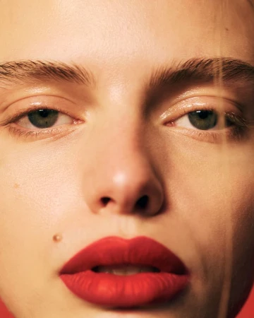 Close-up portrait of a young fair-skinned woman with green eyes and red lipstick, showcasing beauty and cosmetic details.